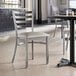 A Lancaster Table & Seating clear coat finish ladder back chair with a light gray vinyl padded seat.