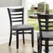 A black Lancaster Table & Seating wood ladder back chair with a light gray vinyl seat at a table in a restaurant.