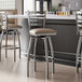 A group of Lancaster Table & Seating ladder back swivel bar stools with taupe vinyl padded seats next to a kitchen counter.
