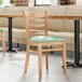 A Lancaster Table & Seating wooden chair with a seafoam vinyl seat in a restaurant.