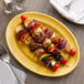 A Tuxton saffron oval china platter with meat and vegetable skewers on it.