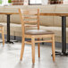 A Lancaster Table & Seating wooden chair with a taupe cushion next to a table in a restaurant.
