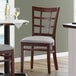 A Lancaster Table & Seating mahogany wood window back chair with a light gray vinyl seat next to a table.