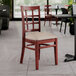 A Lancaster Table & Seating mahogany wood chair with a light gray cushion on a table in a restaurant.