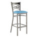 A metal bar stool with a cross back design and a blue vinyl padded seat.