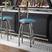 A metal bar stool with a cross back design and a blue vinyl padded seat.