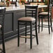 A Lancaster Table & Seating black wood bar stool with a tan vinyl seat.