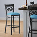 A Lancaster Table & Seating black cross back bar stool with a blue vinyl padded seat.