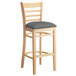 A Lancaster Table & Seating wooden bar stool with a dark gray cushion.