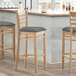 Three Lancaster Table & Seating wood bar stools with dark gray vinyl seats at a counter.