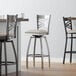 A Lancaster Table & Seating clear coat finish swivel bar stool with a light gray vinyl padded seat.