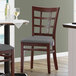 A Lancaster Table & Seating mahogany wood chair with dark gray vinyl seat next to a table.