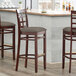 Three Lancaster Table & Seating mahogany wood bar stools with taupe vinyl cushioned seats at a bar counter.