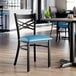 A black metal chair with a cross back design and a blue vinyl padded seat.