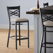 A Lancaster Table & Seating black cross back bar stool with light gray vinyl padded seat.