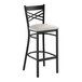 A black metal bar stool with a cross back design and a light gray vinyl padded seat.