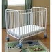 A white L.A. Baby folding crib on a rug.