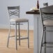 A Lancaster Table & Seating clear coat finish cross back bar stool with a light gray cushion on the seat.