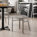A metal cross back chair with a light gray vinyl padded seat and a clear coat finish.