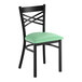 A black metal cross back chair with a 2 1/2 inch seafoam vinyl padded seat.