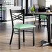 A black metal cross back chair with a 2 1/2 inch seafoam green vinyl padded seat.