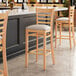 A Lancaster Table & Seating wooden ladder back bar stool with light gray vinyl cushion.