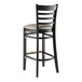 A black wood Lancaster Table & Seating ladder back bar stool with a dark gray vinyl seat.