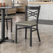 A Lancaster Table & Seating black cross back chair with dark gray vinyl padded seat at a table in a restaurant.