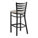 A black metal Lancaster Table & Seating ladder back bar stool with a light gray cushion.