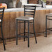 A black metal ladder back bar stool with a light gray vinyl padded seat.