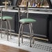 A metal bar stool with a cross back design and a seafoam green vinyl padded seat.
