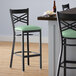 A Lancaster Table & Seating black cross back bar stool with a seafoam green cushion on a table.