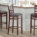 Three Lancaster Table & Seating mahogany wood barstools with dark gray vinyl seats and window backs at a bar counter.