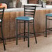 A black ladder back bar stool with a blue vinyl padded seat positioned at a counter.