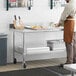 A man standing in a kitchen using a Regency stainless steel work table.