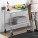 A man in a lab coat standing in front of a Regency stainless steel work table with casters.