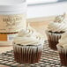 A cupcake with white frosting and vanilla bean paste on a wire rack.