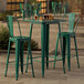 A Lancaster Table & Seating emerald green metal table and chairs on an outdoor patio.