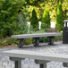 A gray MasonWays plastic park bench with black legs on a brick surface.