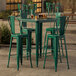 A Lancaster Table & Seating emerald green metal bar table with four green metal chairs.