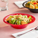 A close up of a red bowl filled with salad on a table.