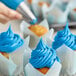 A close up of a person using Rich's Allen Sky Blue Buttrcreme Icing to decorate a cupcake.