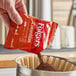 A packet of Folgers Colombian Supreme ground coffee being poured into a coffee filter.
