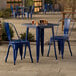 A Lancaster Table & Seating blue metal table with 2 blue chairs on an outdoor patio.