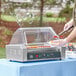 A person putting hot dogs into a Carnival King hot dog roller grill on a counter.