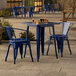 A blue metal Lancaster Table & Seating outdoor table and chairs on a stone patio.