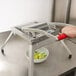 A hand with a red handle using a Vollrath lettuce slicer over a bowl of lettuce.