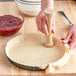 A person using a Fox Run rubberwood tart tamper to make a pie crust.
