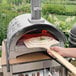 A person putting a pizza into a WPPO stainless steel wood fire pizza oven.