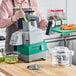 A person using an AvaMix commercial food processor with a clear bowl to cut vegetables.